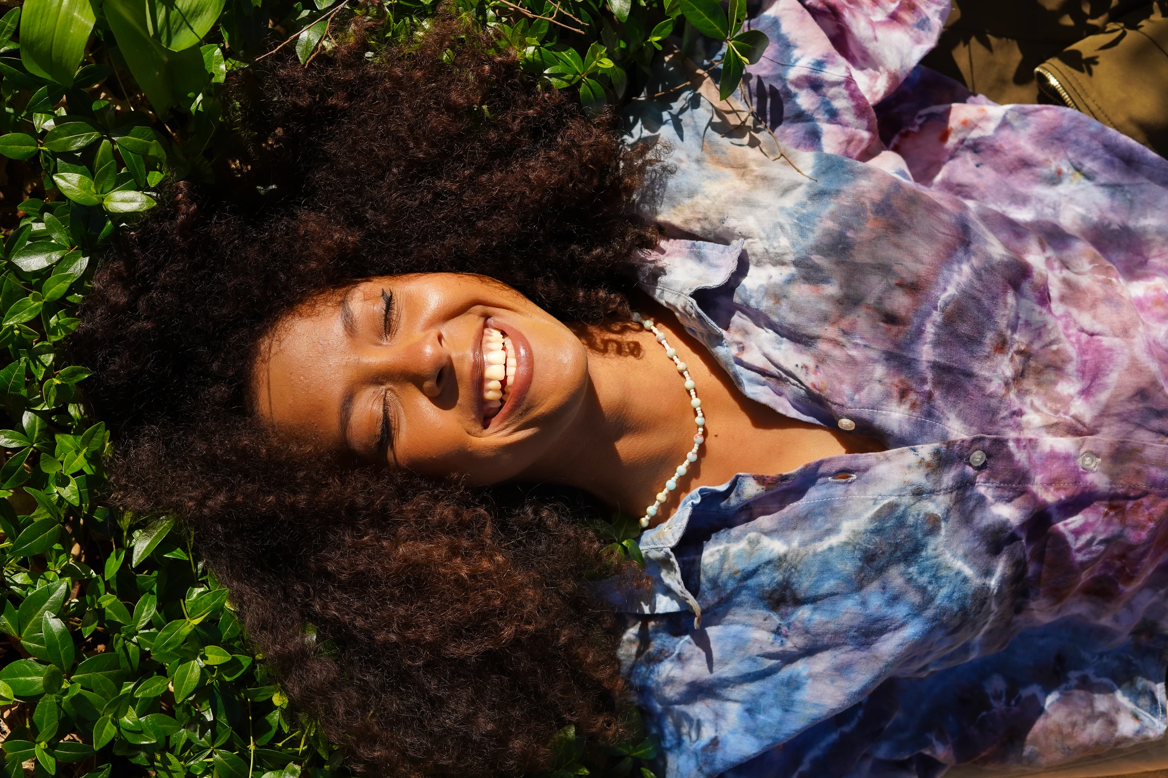 Sunlit lifestyle portrait of a woman lying in greenery by Lunar Lens Creative Agency