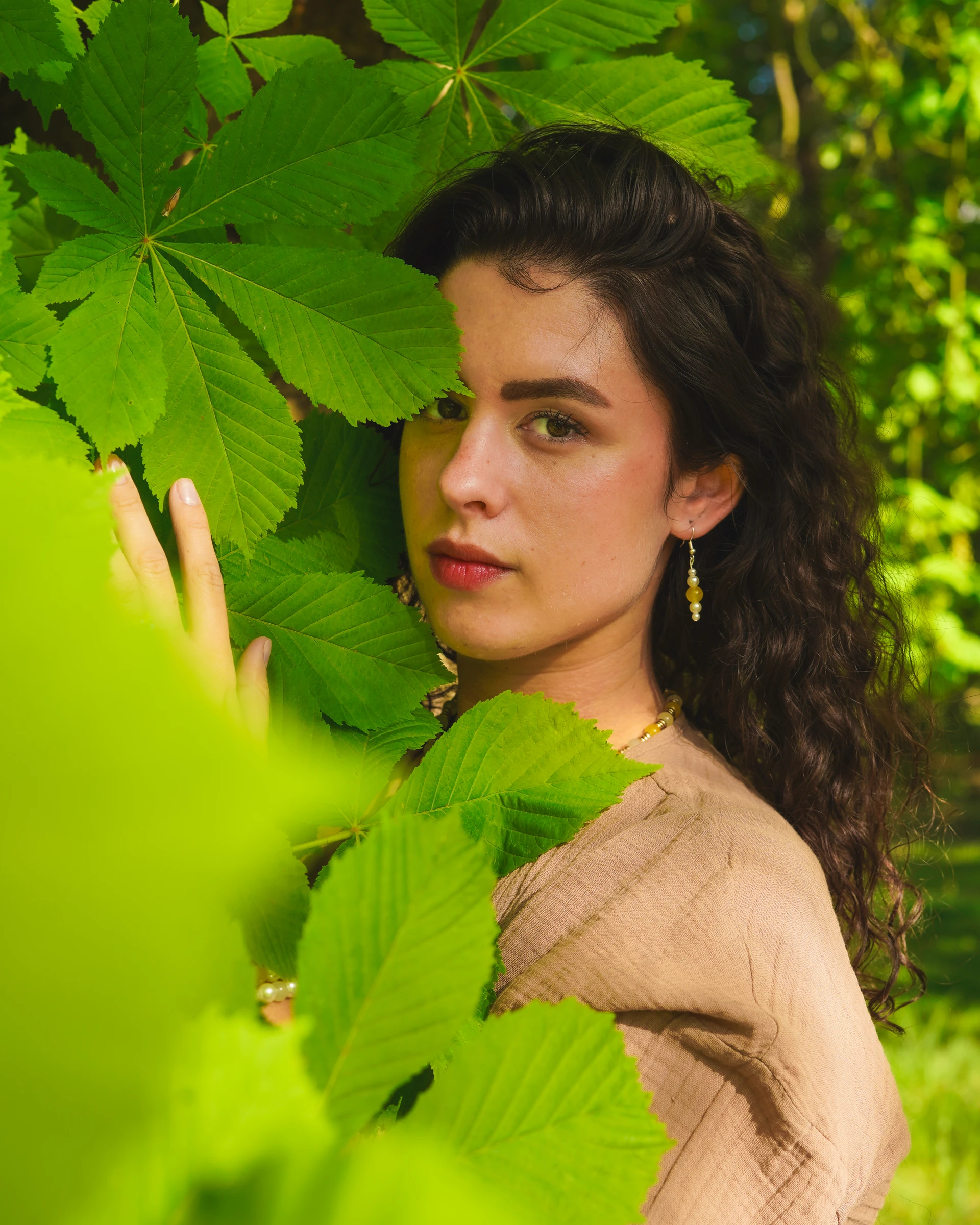 Outdoor portrait of a woman framed by green leaves by Lunar Lens Creative Agency